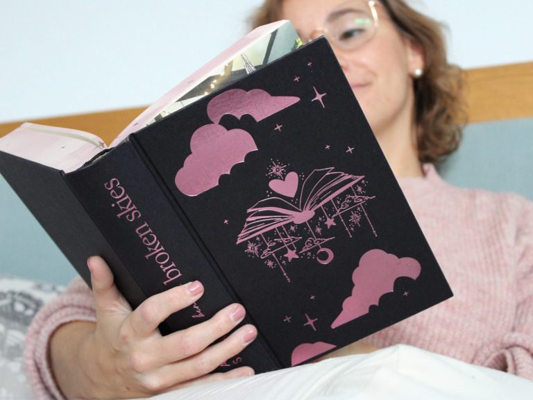 Frau liest ein schwarzes Buch mit pinkem Cover in einem gemütlichen Raum.