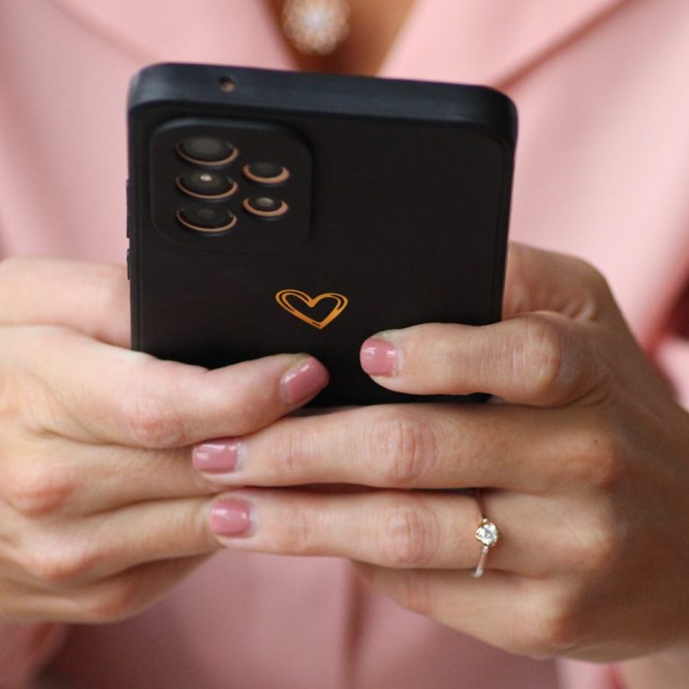 Hände halten ein Smartphone mit einem Herz-Muster auf der Rückseite.