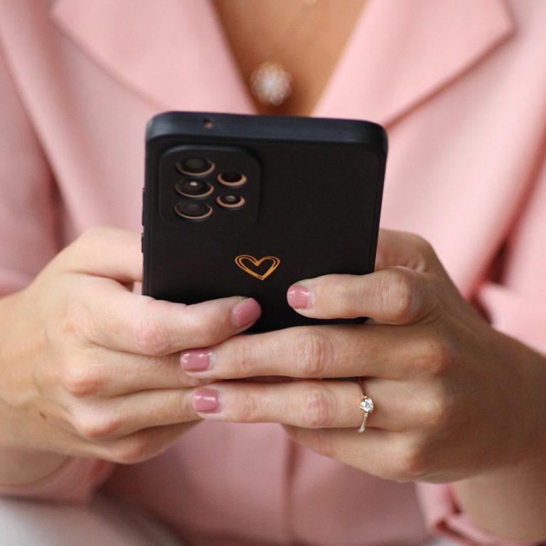 Hände einer Person mit einem Smartphone, das ein herzförmiges Symbol zeigt.