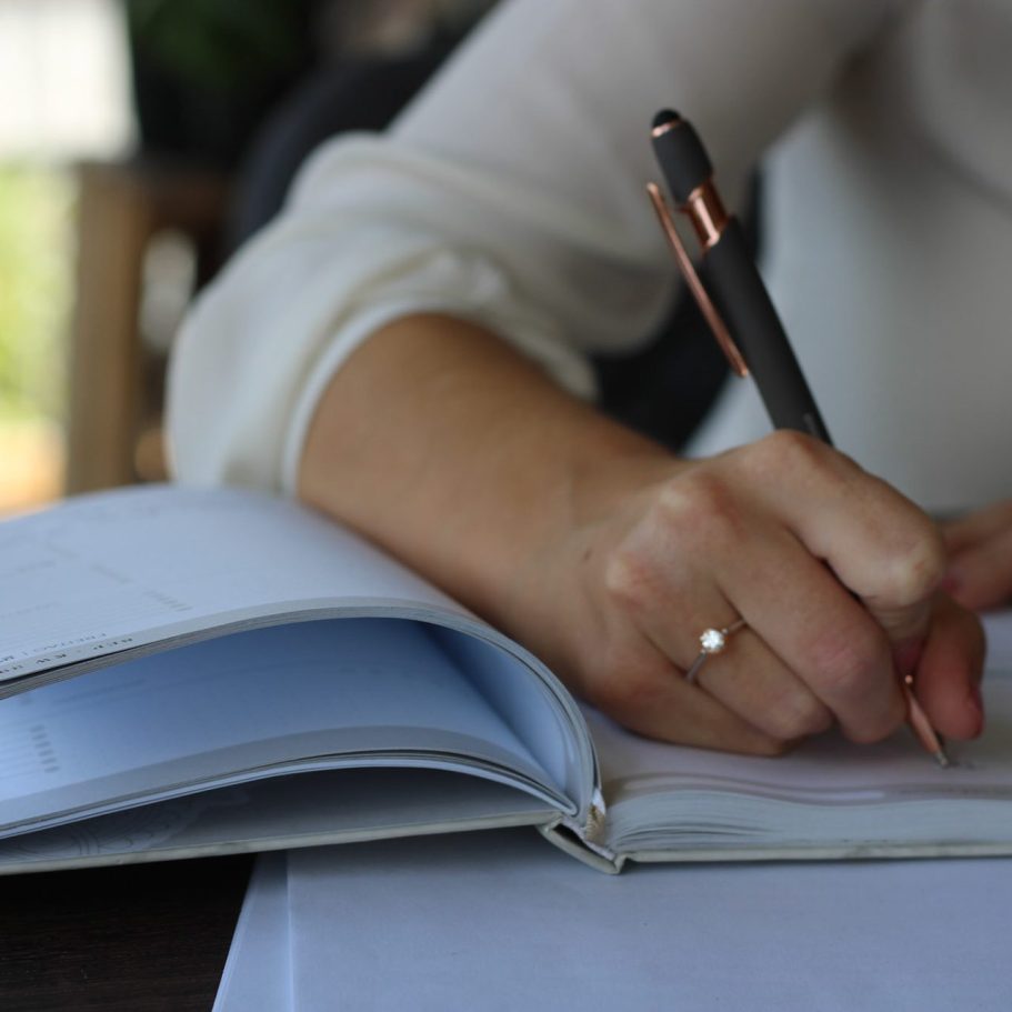 Eine Hand schreibt mit einem Stift in ein offenes Notizbuch.
