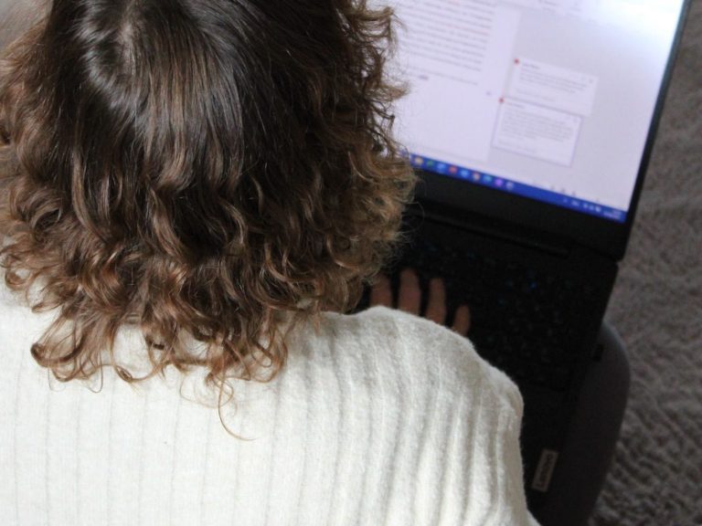 Person mit lockigem Haar tippt auf einem Laptop.